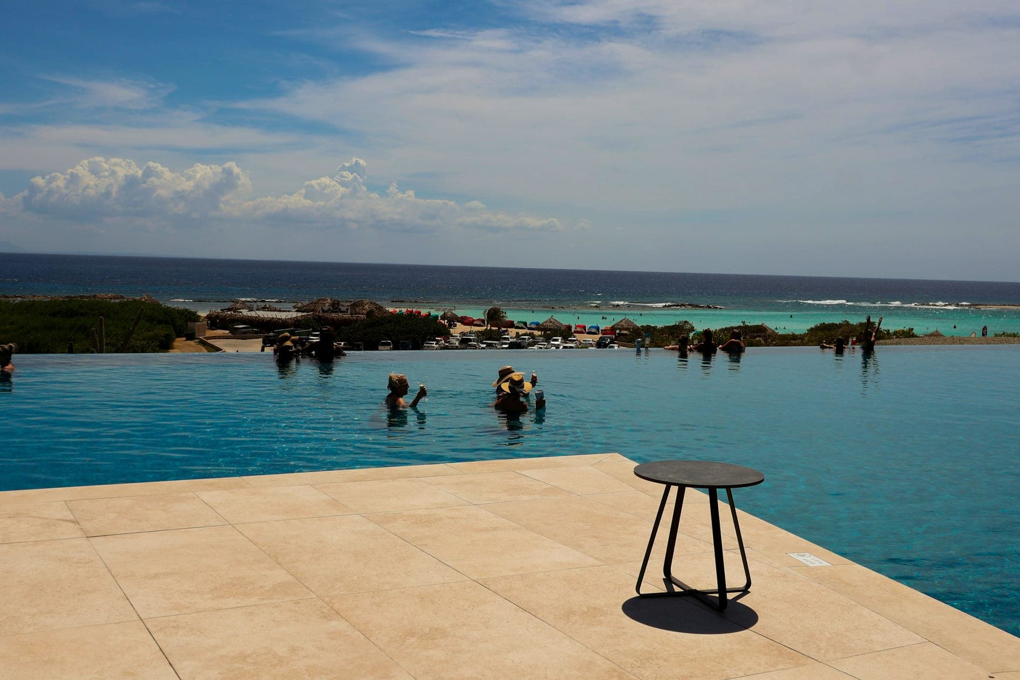 Swimmers in an infinity pool with a panoramic ocean view beyond